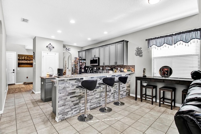 kitchen with kitchen peninsula, appliances with stainless steel finishes, decorative backsplash, a kitchen breakfast bar, and gray cabinets