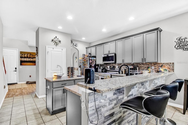 kitchen with gray cabinetry, a center island with sink, light stone countertops, and appliances with stainless steel finishes