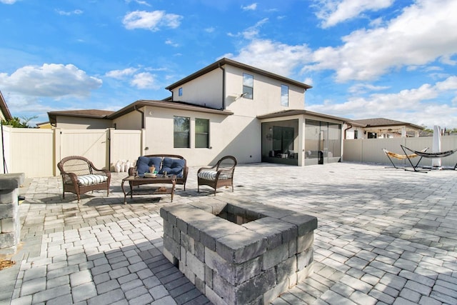 back of house featuring a sunroom, a patio area, and an outdoor living space with a fire pit