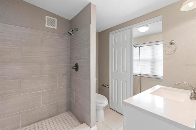 bathroom with a tile shower, vanity, toilet, and tile patterned floors