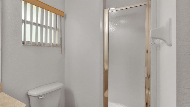 bathroom featuring a shower with door and toilet