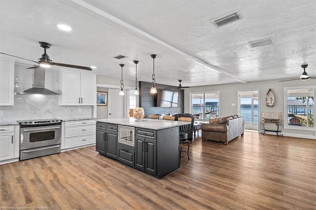 kitchen featuring white cabinetry, stainless steel appliances, wall chimney range hood, and wood-type flooring