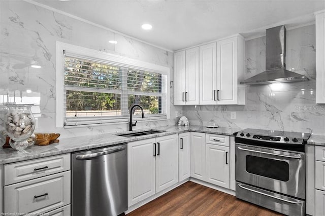 kitchen featuring white cabinetry, wall chimney range hood, sink, and appliances with stainless steel finishes