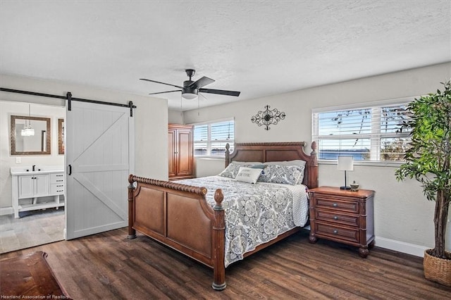 bedroom with a barn door, multiple windows, dark wood-type flooring, and connected bathroom