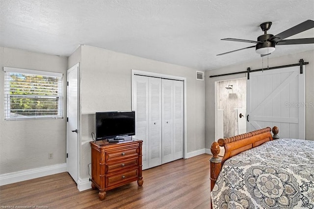 bedroom with a textured ceiling, ceiling fan, a barn door, hardwood / wood-style flooring, and a closet