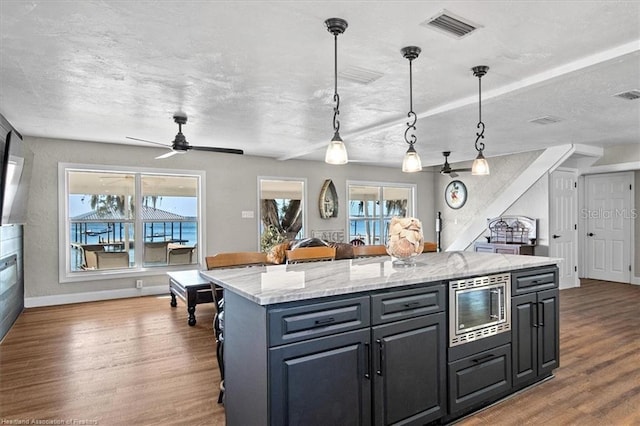 kitchen featuring hardwood / wood-style flooring, decorative light fixtures, stainless steel microwave, and plenty of natural light