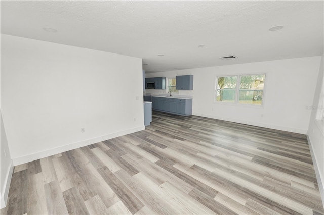 unfurnished living room featuring a textured ceiling, light hardwood / wood-style flooring, and sink