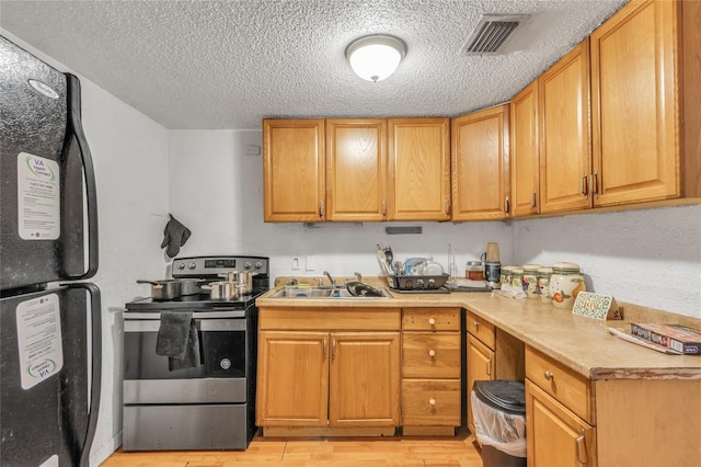 kitchen with sink, light hardwood / wood-style flooring, a textured ceiling, stainless steel range with electric stovetop, and black refrigerator