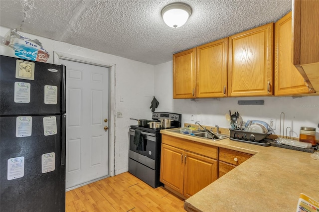 kitchen featuring electric range, sink, light hardwood / wood-style flooring, a textured ceiling, and black refrigerator