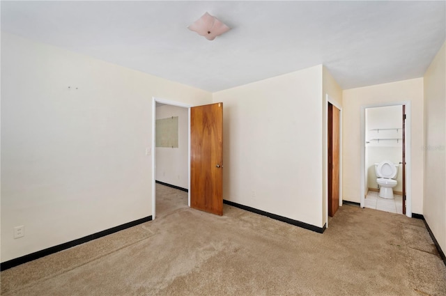 unfurnished bedroom with ensuite bathroom, a closet, and light colored carpet