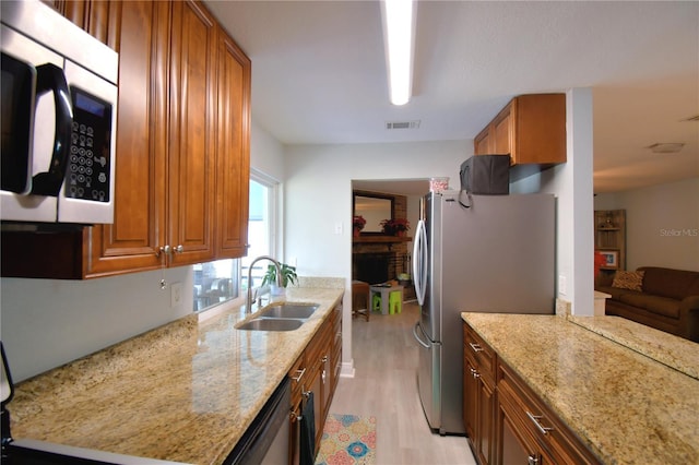 kitchen featuring appliances with stainless steel finishes, light hardwood / wood-style floors, light stone counters, and sink