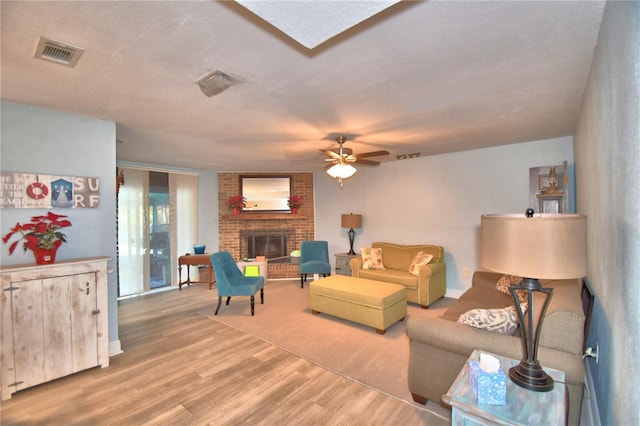 living room featuring a fireplace, ceiling fan, wood-type flooring, and a textured ceiling