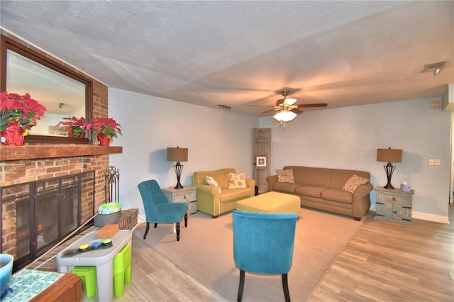 living room featuring ceiling fan, hardwood / wood-style floors, a textured ceiling, and a brick fireplace