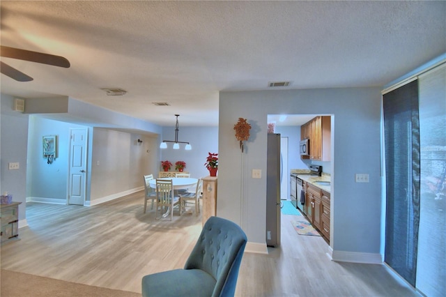 dining area with ceiling fan, light hardwood / wood-style floors, and a textured ceiling