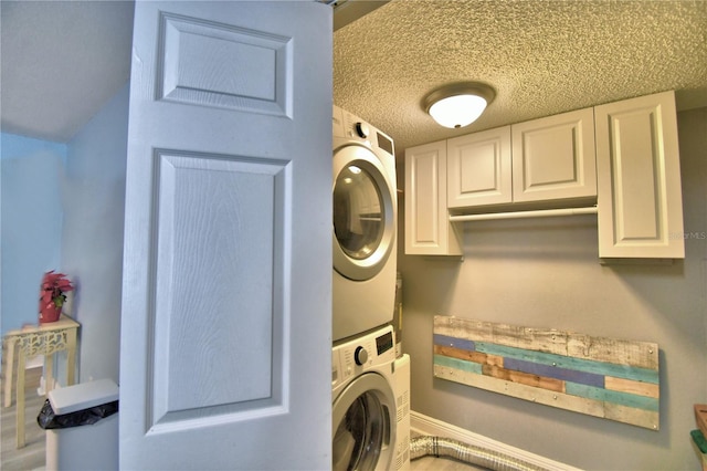 washroom with cabinets, a textured ceiling, and stacked washer and clothes dryer