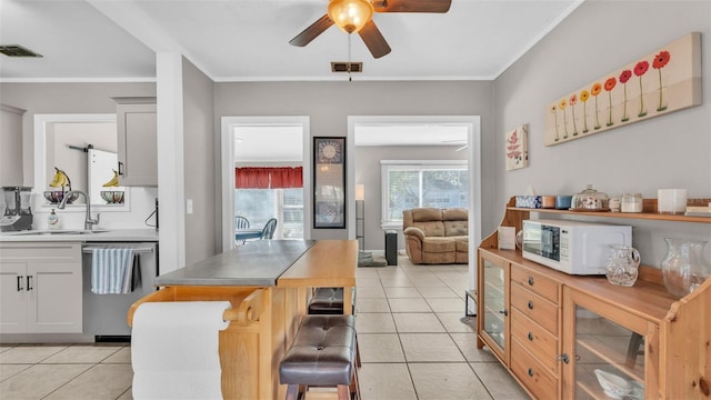 kitchen featuring sink, light tile patterned floors, dishwasher, ceiling fan, and a kitchen breakfast bar