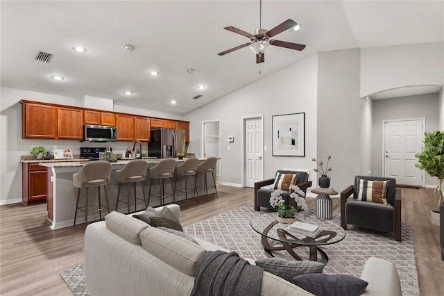 living room with light wood-type flooring, high vaulted ceiling, ceiling fan, and sink