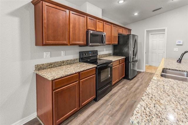 kitchen with lofted ceiling, sink, light hardwood / wood-style flooring, appliances with stainless steel finishes, and light stone counters