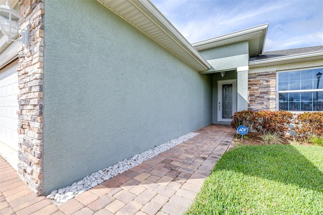 view of exterior entry with an attached garage, stone siding, and stucco siding