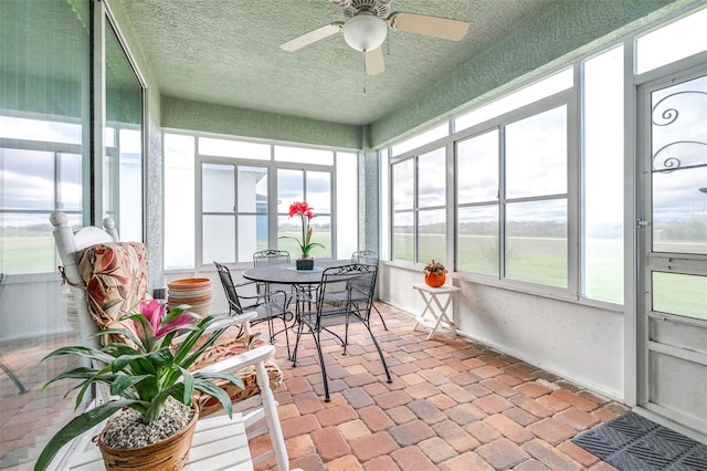 sunroom featuring a ceiling fan, a textured ceiling, and outdoor dining space