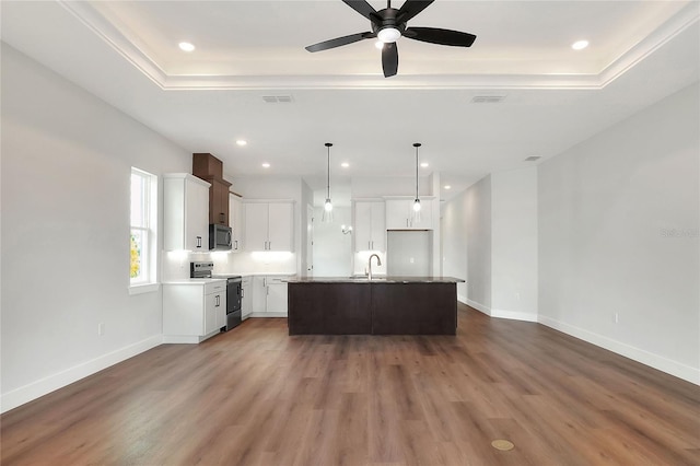 kitchen with appliances with stainless steel finishes, sink, wood-type flooring, white cabinets, and an island with sink