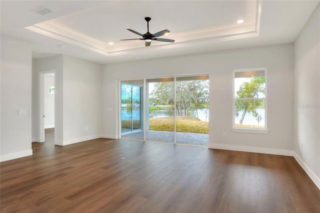 empty room with a raised ceiling, ceiling fan, and dark hardwood / wood-style floors