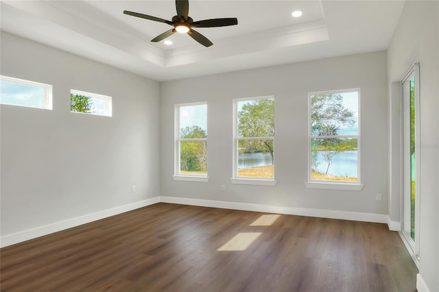 unfurnished room featuring a tray ceiling, ceiling fan, hardwood / wood-style floors, and a water view