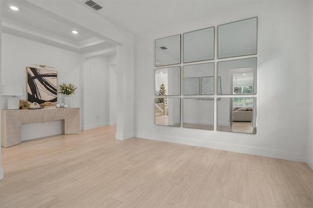 empty room featuring light wood-type flooring, a raised ceiling, and crown molding