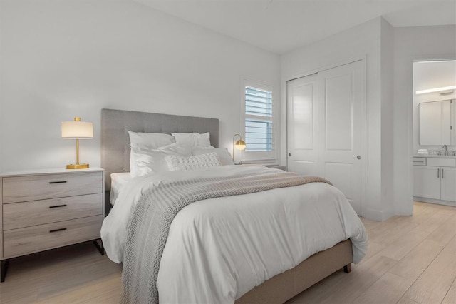 bedroom with light wood-type flooring, connected bathroom, a closet, and sink