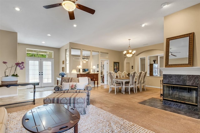 carpeted living room with ceiling fan with notable chandelier, a tiled fireplace, and french doors