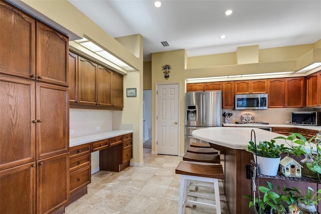 kitchen with backsplash, a breakfast bar, built in desk, and stainless steel appliances