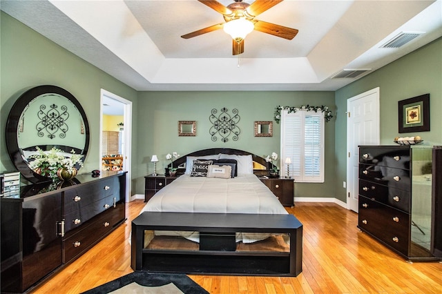 bedroom featuring ceiling fan, a raised ceiling, and light hardwood / wood-style flooring