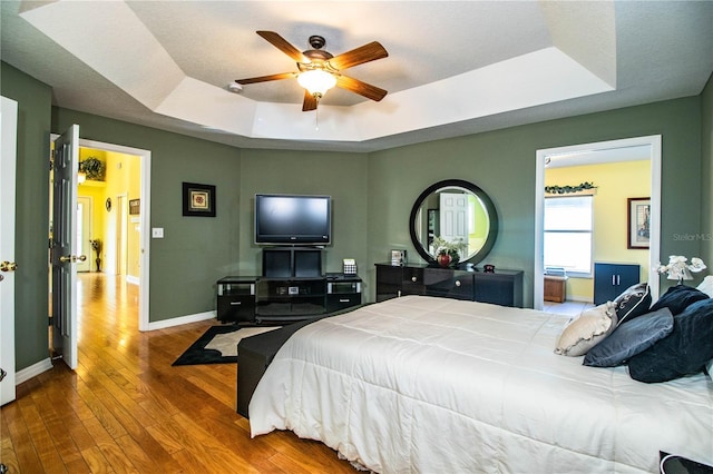 bedroom with wood-type flooring, a raised ceiling, and ceiling fan