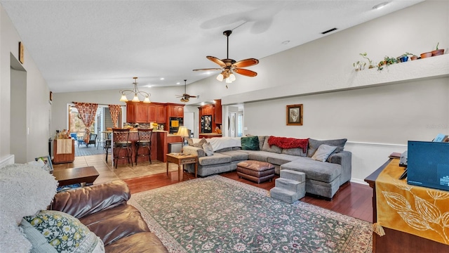 living room featuring ceiling fan with notable chandelier, light hardwood / wood-style floors, and vaulted ceiling