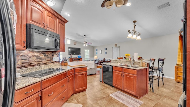 kitchen with hanging light fixtures, light stone counters, lofted ceiling, decorative backsplash, and black appliances