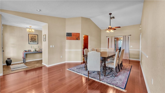 dining space with ceiling fan with notable chandelier, hardwood / wood-style flooring, and vaulted ceiling