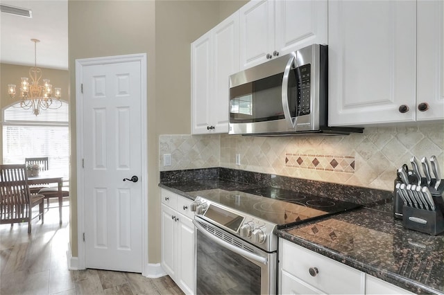 kitchen with appliances with stainless steel finishes, dark stone counters, an inviting chandelier, white cabinets, and hanging light fixtures