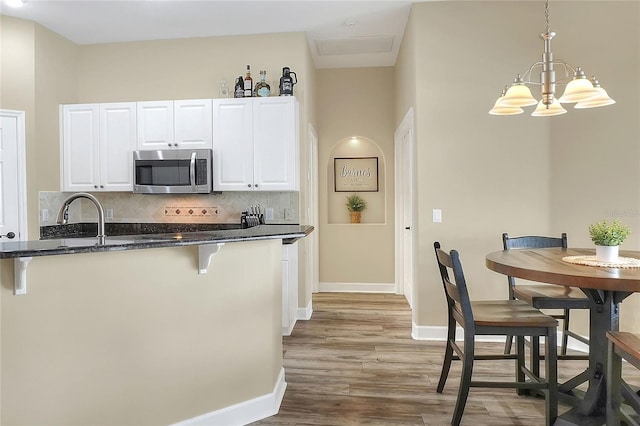 kitchen with decorative backsplash, white cabinets, pendant lighting, and an inviting chandelier