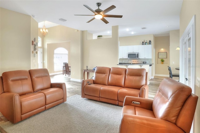 living room with ceiling fan with notable chandelier, light wood-type flooring, and sink