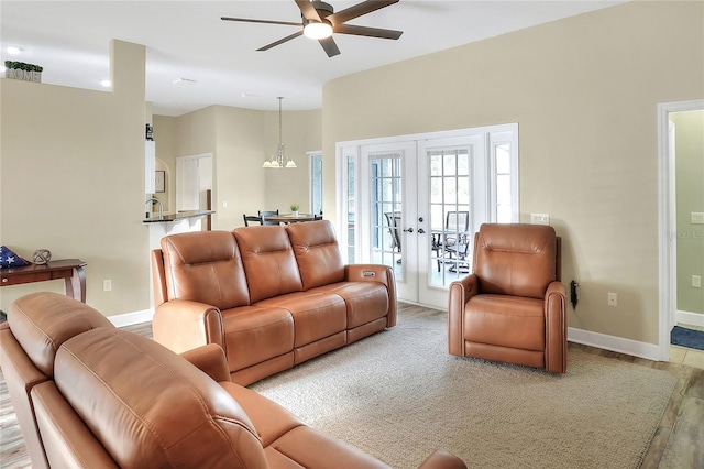 living room featuring ceiling fan with notable chandelier, wood-type flooring, and french doors