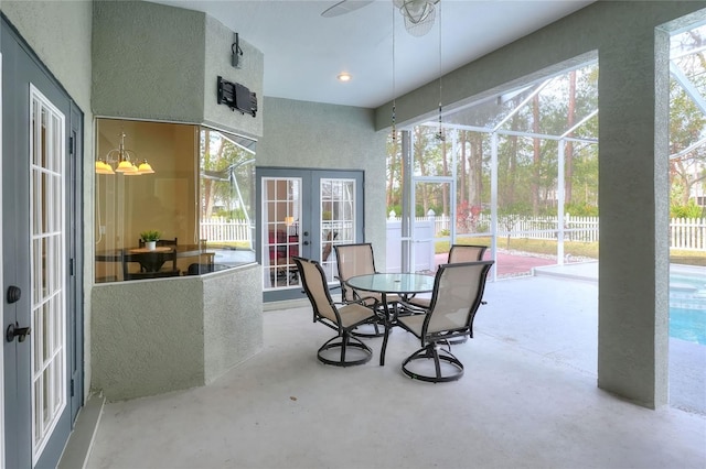 sunroom / solarium featuring ceiling fan with notable chandelier and french doors