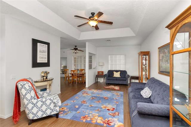 living room featuring a textured ceiling, a tray ceiling, ceiling fan, and dark wood-type flooring