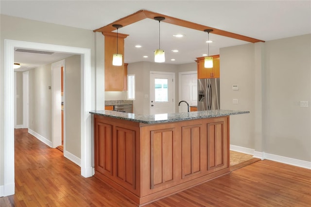 kitchen with dark stone counters, sink, decorative light fixtures, light hardwood / wood-style flooring, and stainless steel fridge with ice dispenser