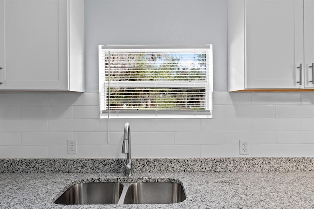 kitchen featuring light stone countertops, tasteful backsplash, white cabinets, and sink