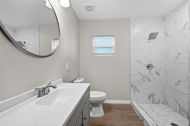 bathroom with hardwood / wood-style flooring, vanity, toilet, and a tile shower