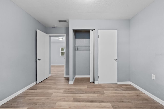 unfurnished bedroom featuring a closet, a textured ceiling, and light hardwood / wood-style flooring