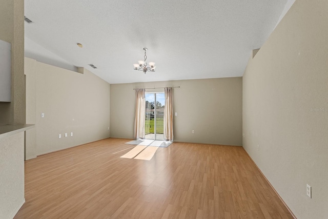 empty room featuring lofted ceiling, light hardwood / wood-style flooring, a textured ceiling, and an inviting chandelier