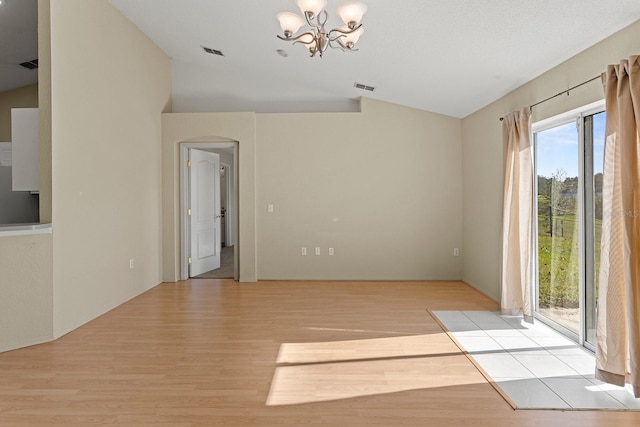 spare room featuring light wood-type flooring, vaulted ceiling, and a notable chandelier