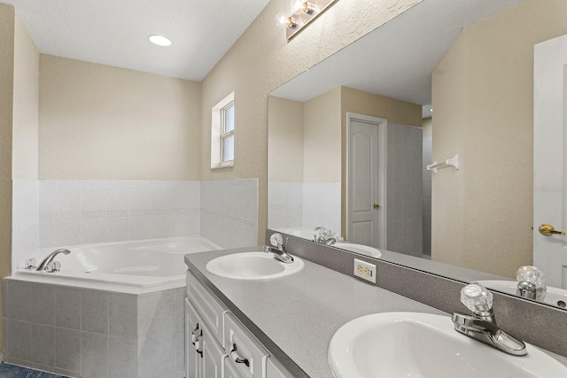 bathroom featuring a textured ceiling, vanity, and tiled bath