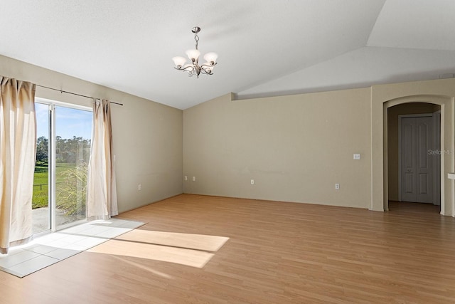 empty room featuring a notable chandelier, lofted ceiling, and light wood-type flooring